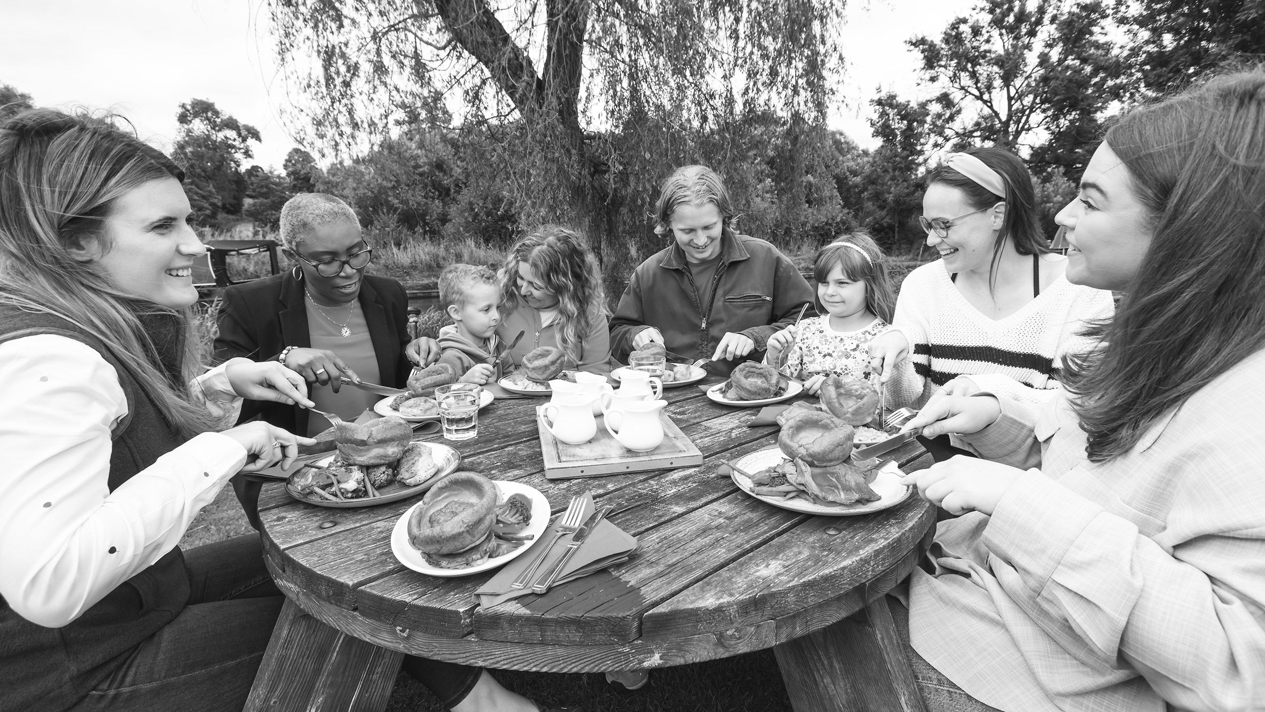 A black and white image of a group of children and adults sat outside enjoying beef meals