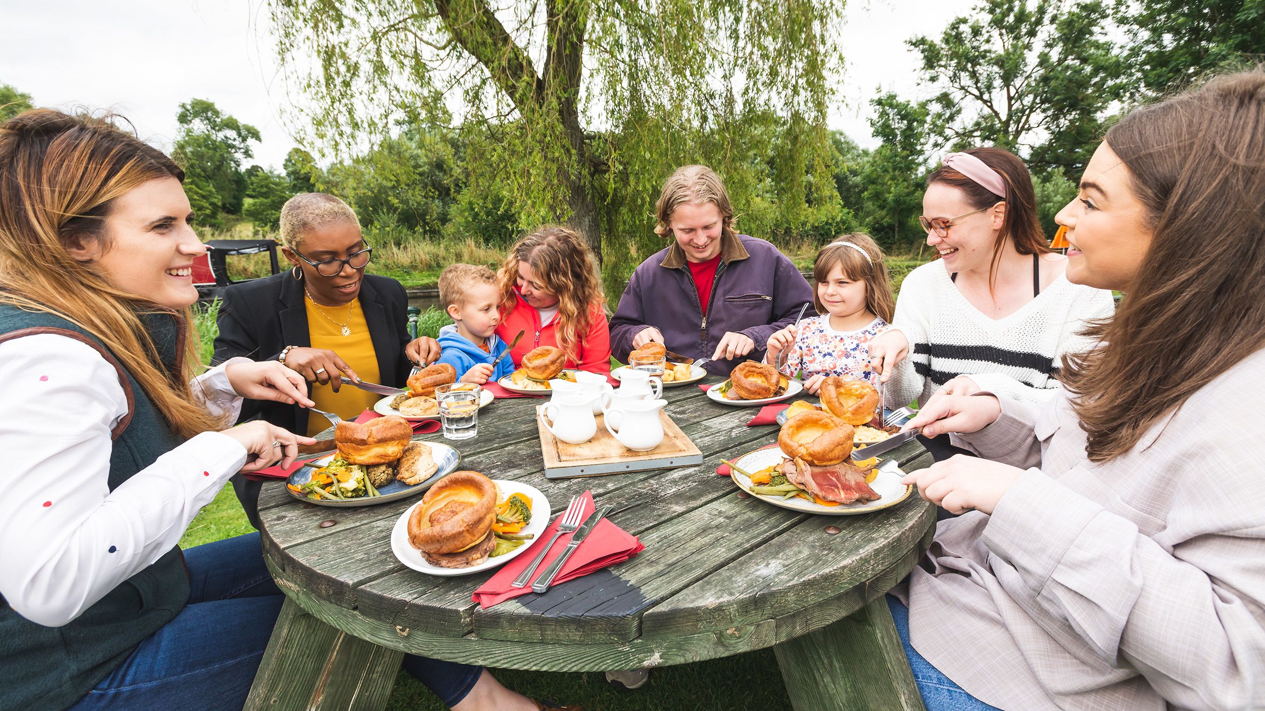 A group of children and adults sat outside enjoying beef meals