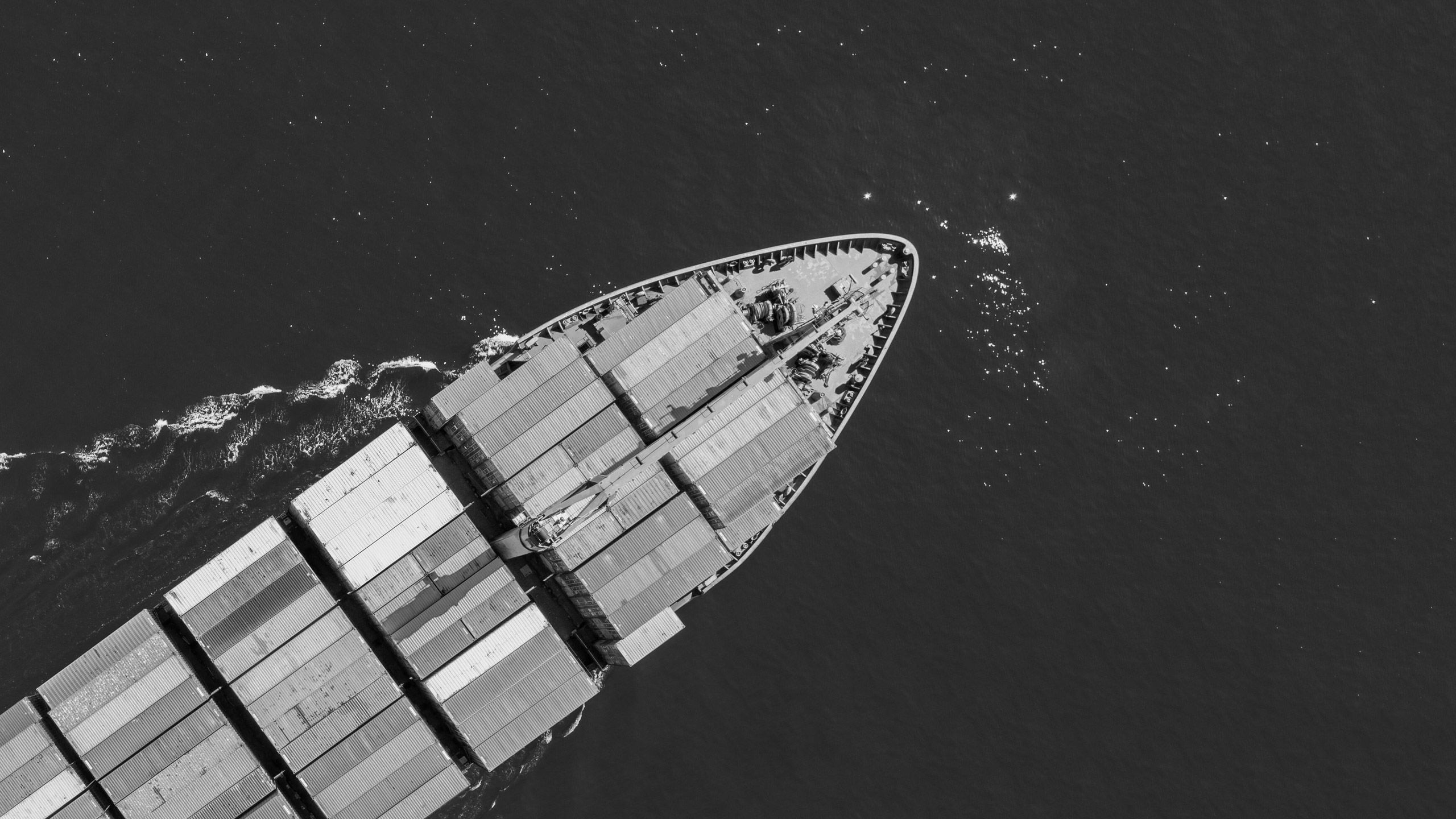 An ariel view of a cargo ship sailing through the ocean, pictured in black and white