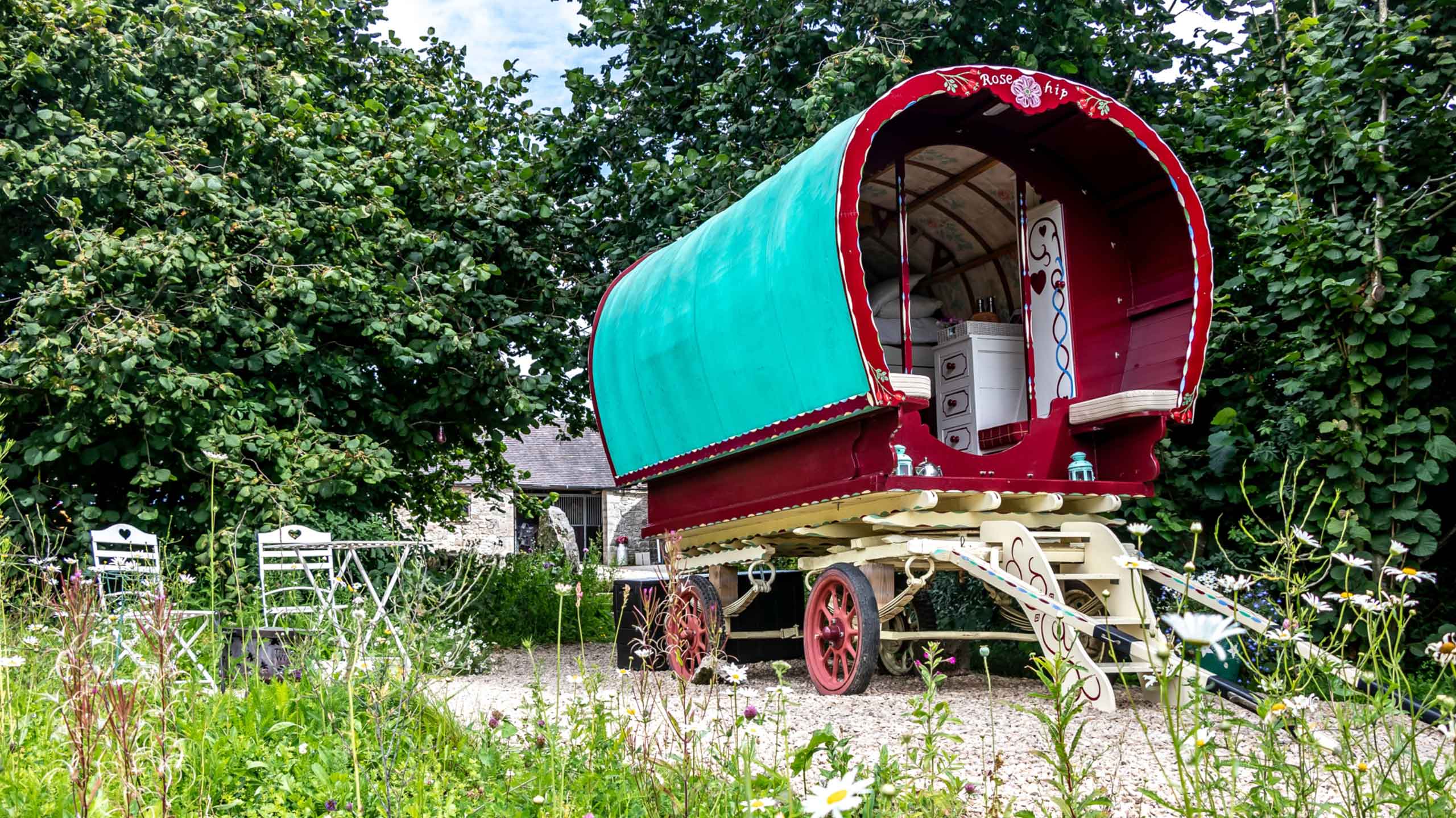 A Romany caravan situated in a field with a table and chairs